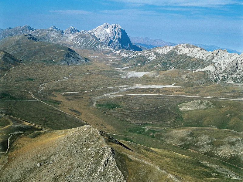 Aerial view of the Campo Imperatore plateau, with pastures and dirt roads and Corno Grande in the background