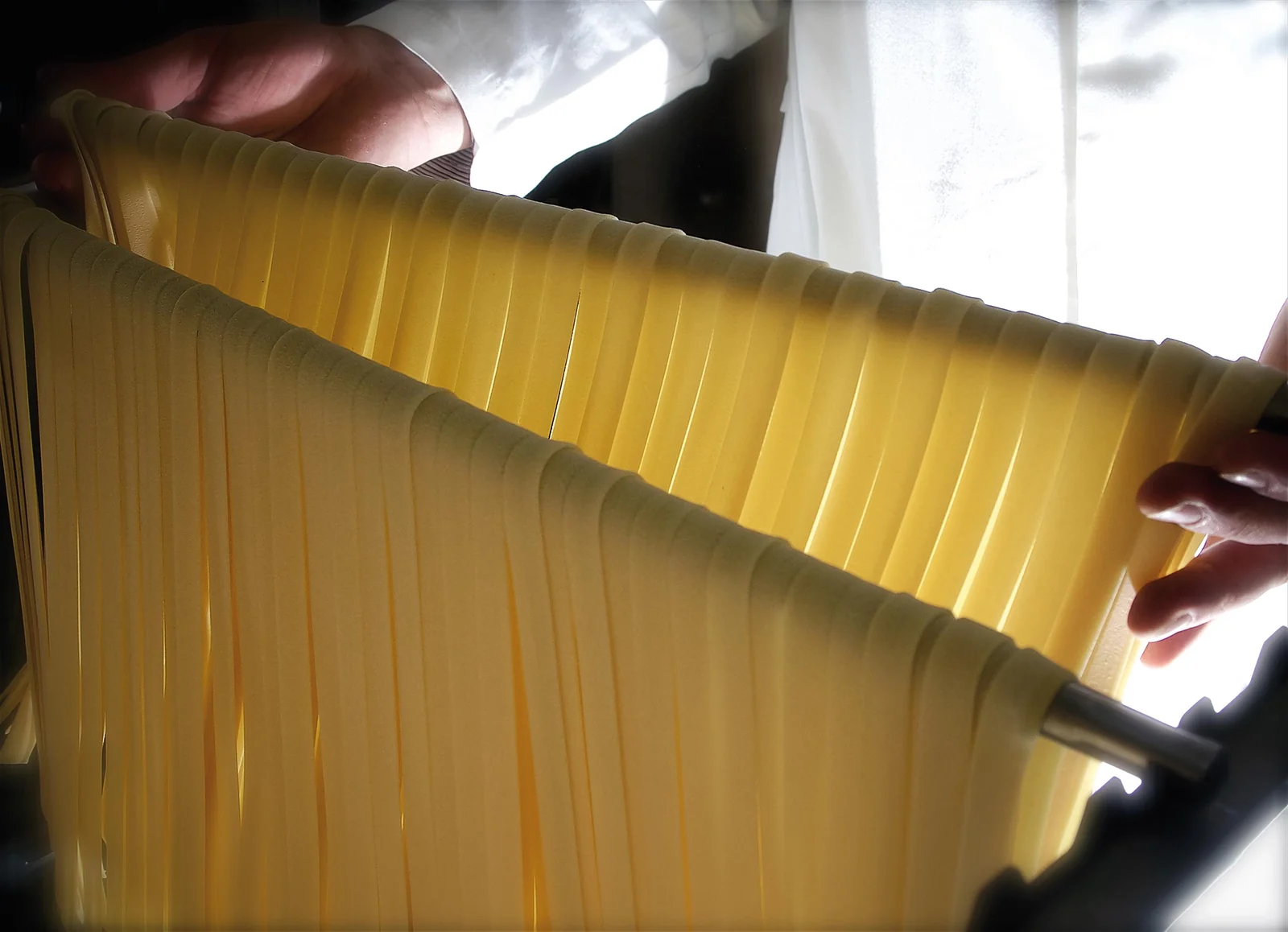 Hands and long pasta hanging on supports at Pastificio Gentile